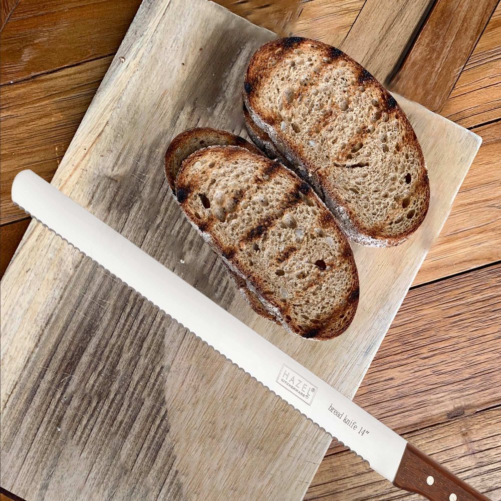 The bread knife laid on a wooden cutting board next to two toasted bread slices.