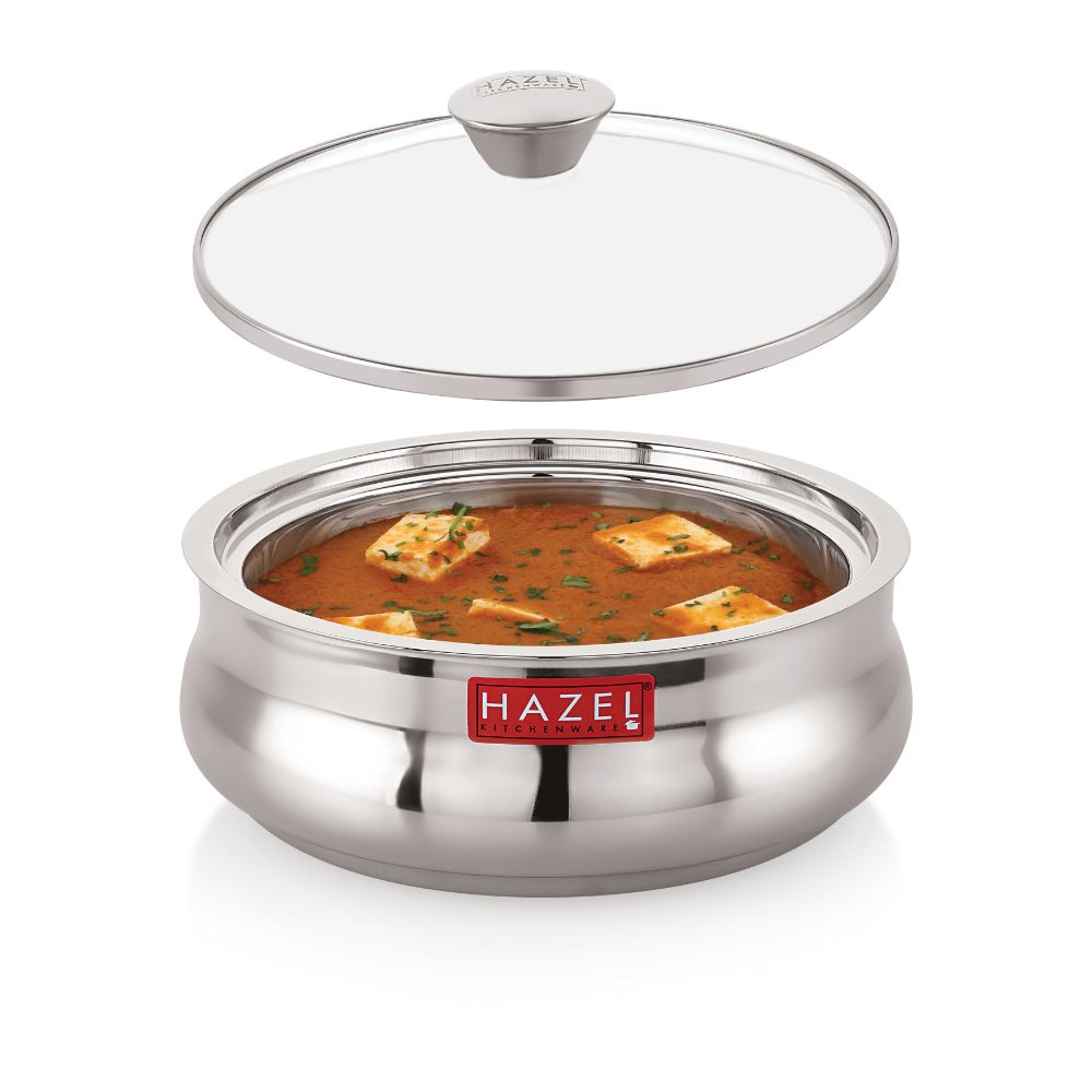 Casserole filled with paneer curry with its glass lid detached and floating above it, on a white background.