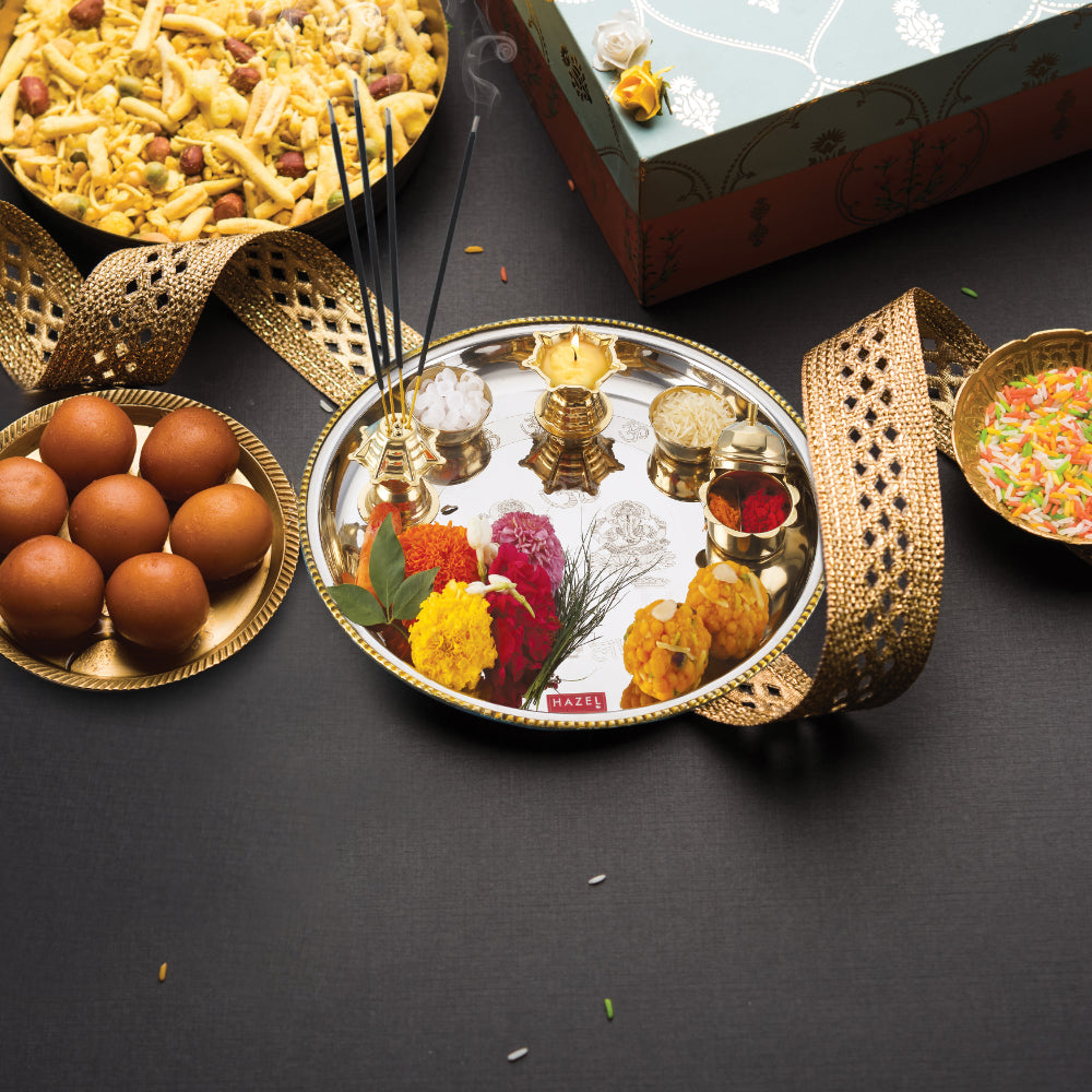 Styled pooja thali with flowers and incense placed beside laddoos, a decorative box, and golden ribbon on a dark background.