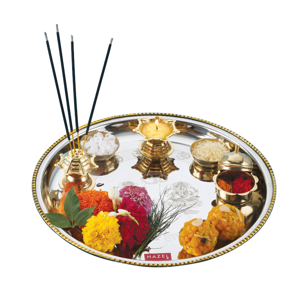 Styled pooja thali with lit diya, incense sticks, and marigold flowers on a white background.