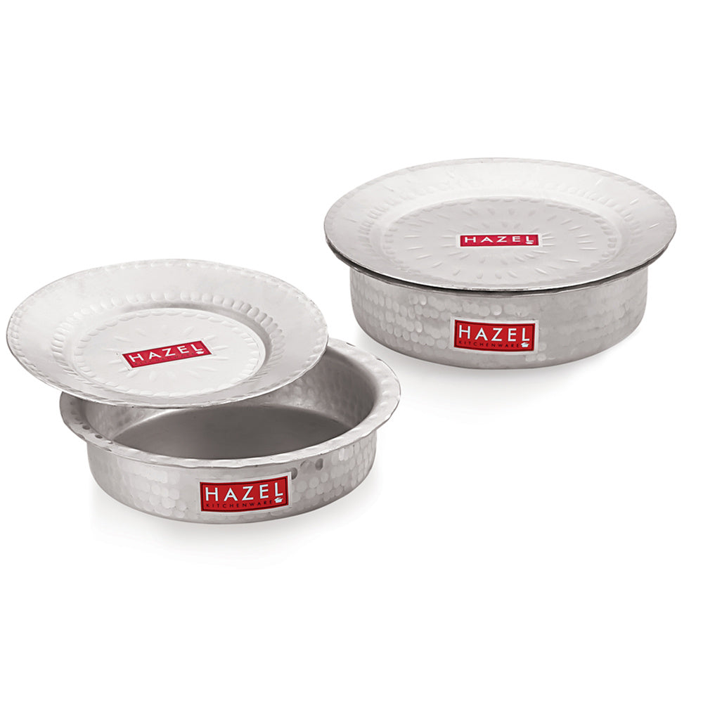 Set of aluminium hammered patilas with lids in two sizes, stacked and arranged together on a white background.