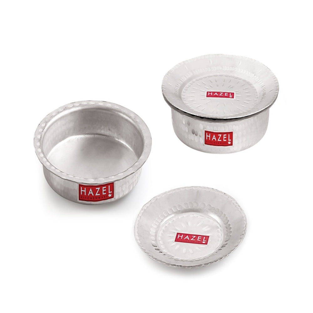 Two hammered aluminium patilas and a lid arranged together on a white background.