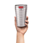 A hand holding a single steel jumbo glass to show scale.