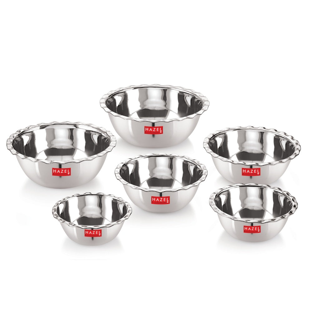 Six scalloped stainless steel serving bowls arranged in a group on a white background.