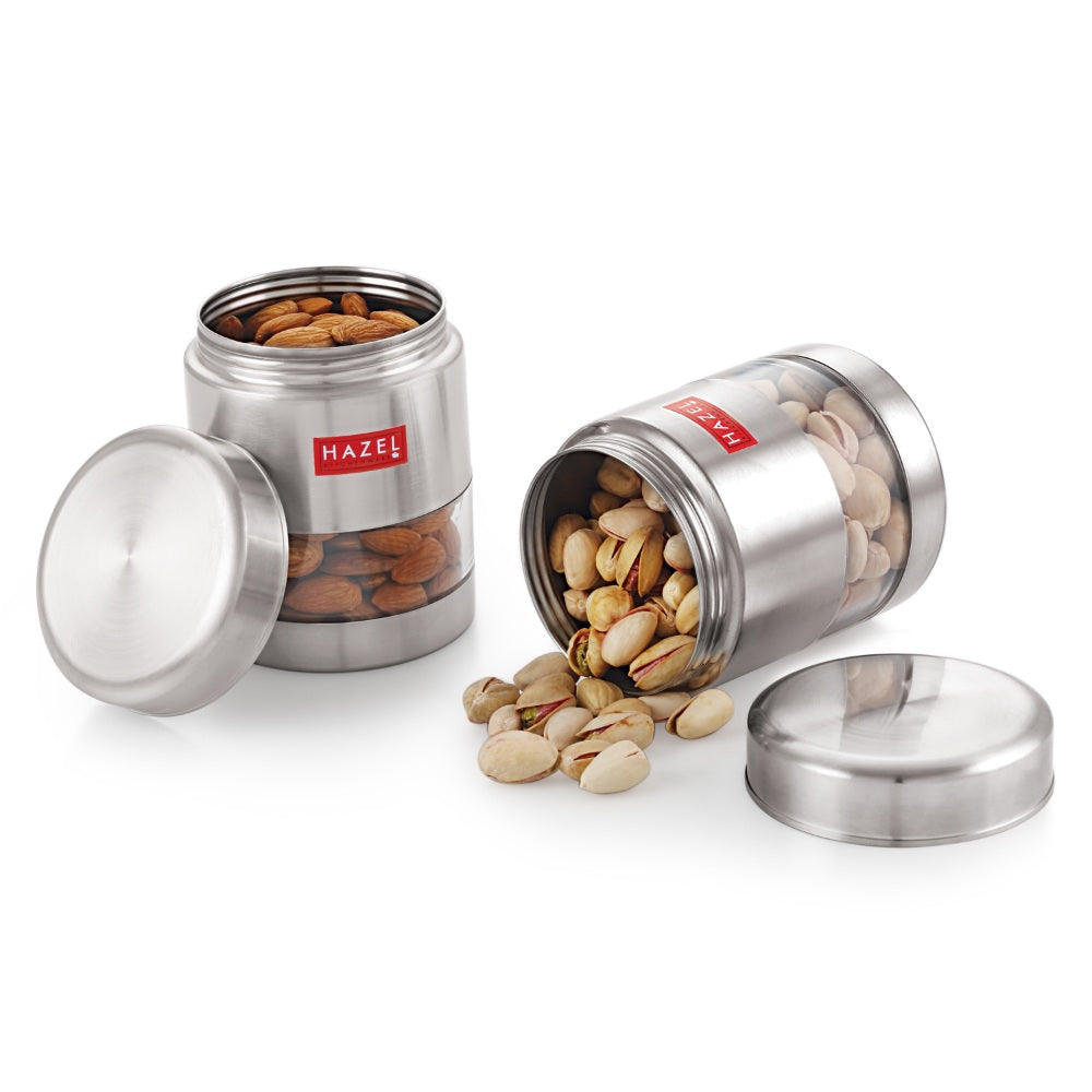Two open containers with nuts and pistachios spilling near their loose lids on white.