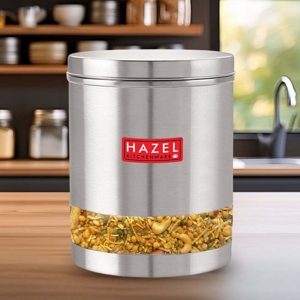 Container filled with sprouted grains standing on a wooden kitchen counter with shelves and a sink in the background.