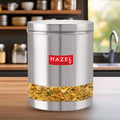 Container filled with sprouted grains standing on a wooden kitchen counter with shelves and a sink in the background.