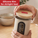 Hands holding a white canister with a wooden lid, silicone rim and oval viewing window
