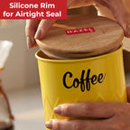Hands lifting the wooden lid off the yellow coffee canister with red 'Silicone Rim Airtight Seal' text.