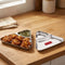 Stainless steel triangular two-section plate beside pakoras and green chutney on a wooden counter