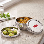 Open lunch box filled with curry next to a small divided plate with food and a separate lid, on a white background.