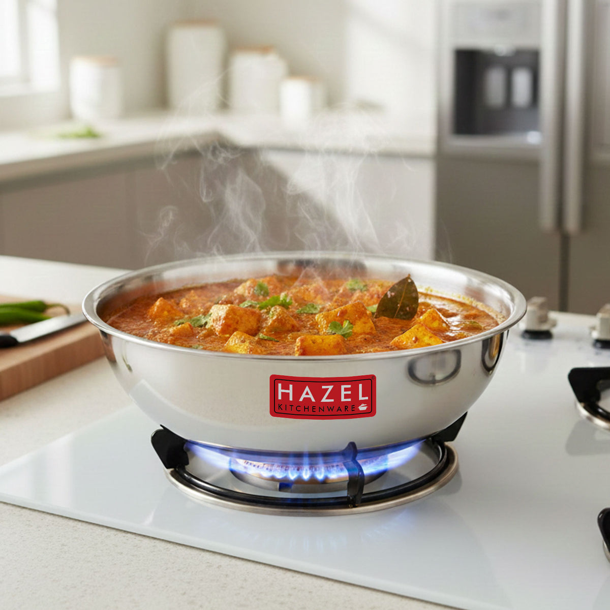 Steel tasra filled with steaming vegetable curry, sitting on a lit gas stove burner in a kitchen.