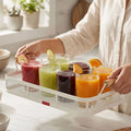Person placing fruit into the white mesh basket tray of apples, grapes and orange, hands visible over a marble counter.